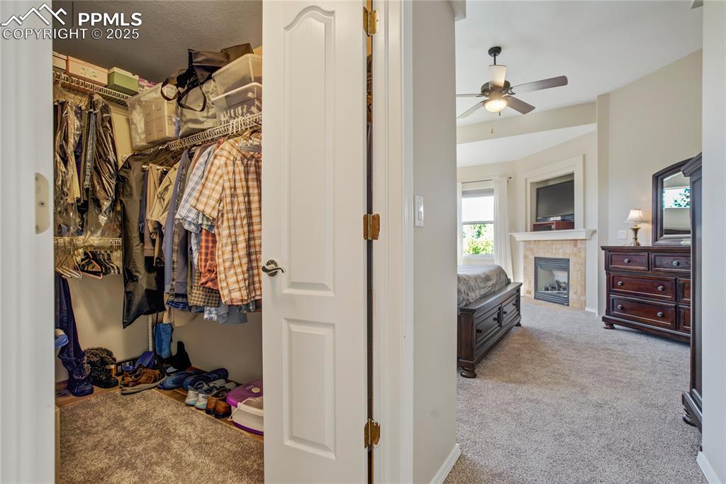 Image 22 of 43: Spacious closet with light carpet, a tiled fireplace, and a ceiling fan
