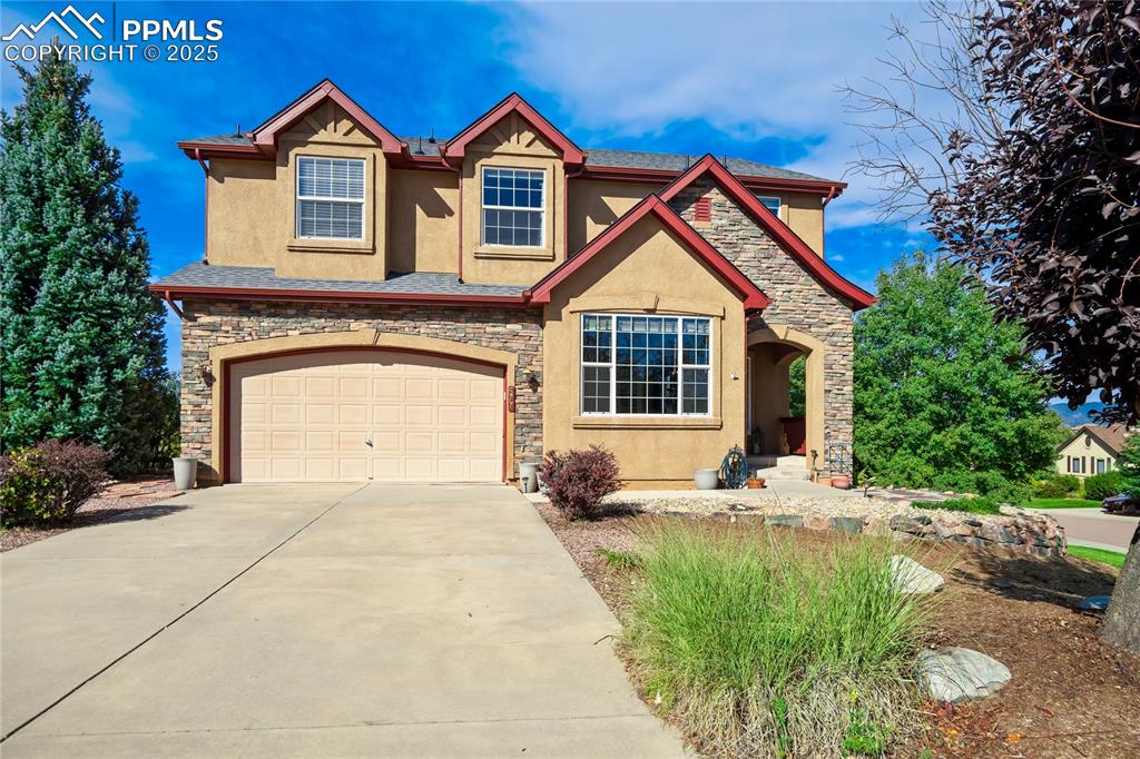 Image 42 of 43: View of front of house with stone siding, stucco siding, driveway, and an a