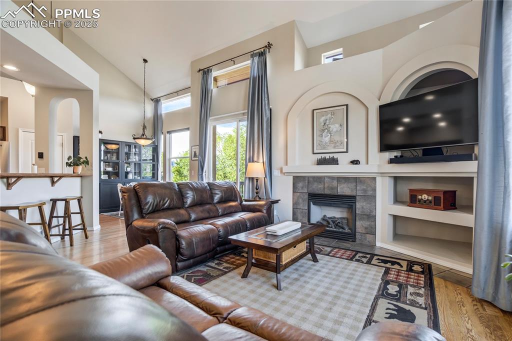 Image 5 of 43: Living area with wood finished floors, a fireplace, a towering ceiling, and