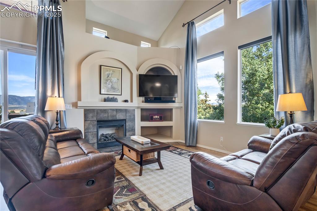 Image 6 of 43: Living room featuring a tiled fireplace, high vaulted ceiling, and wood fin