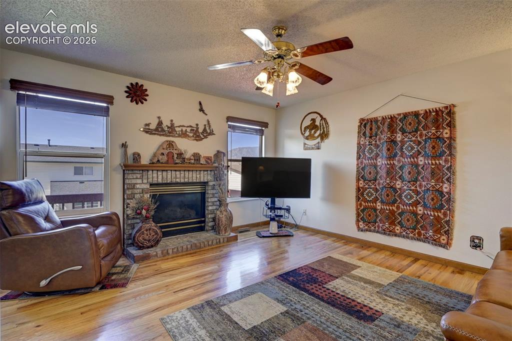 Image 16 of 50: Family Room with fireplace, ceiling fan and wood flooring.