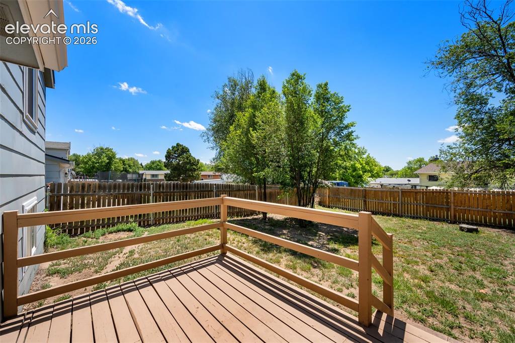 Image 30 of 39: Wood-finish deck with a perimeter railing overlooking a fenced backyard