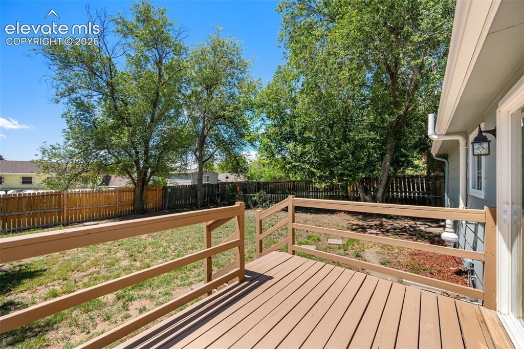 Image 31 of 39: Spacious wood-finish deck overlooking a fenced backyard with mature trees