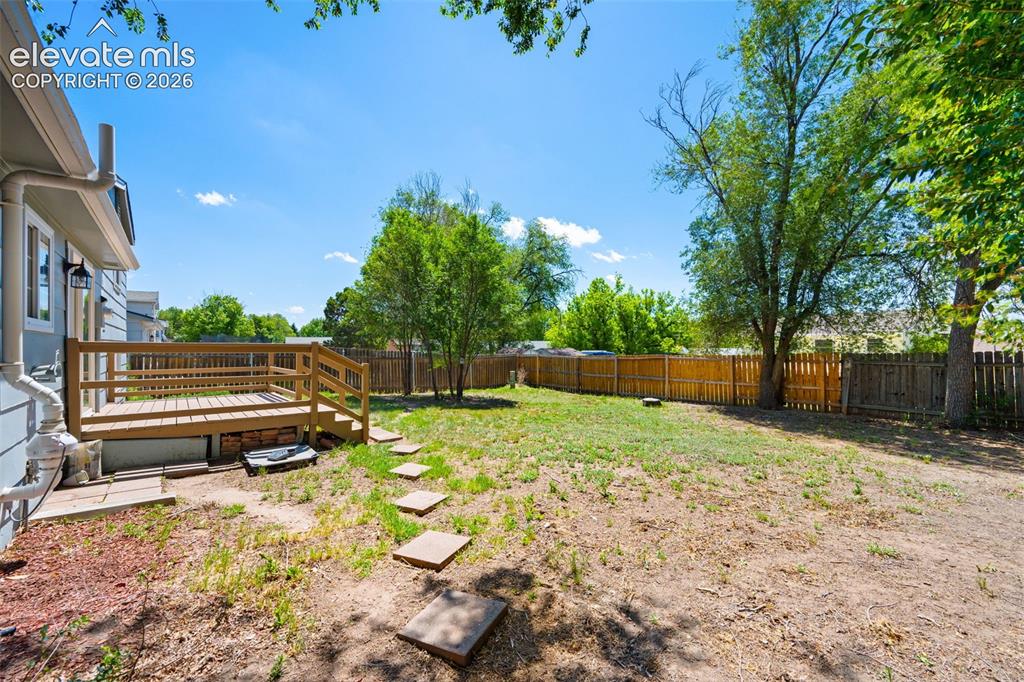 Image 32 of 39: Spacious backyard featuring a wooden deck with railing, stepping stones, ma