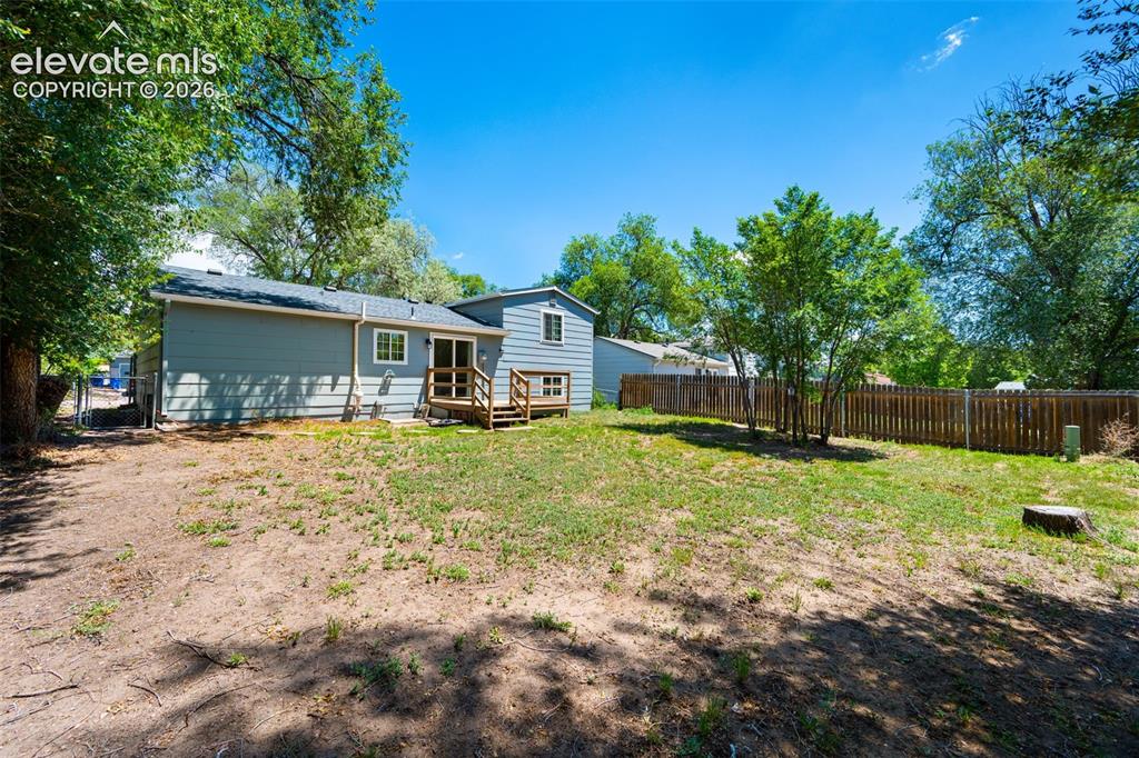 Image 33 of 39: Expansive backyard featuring a partial wooden privacy fence, mature trees,