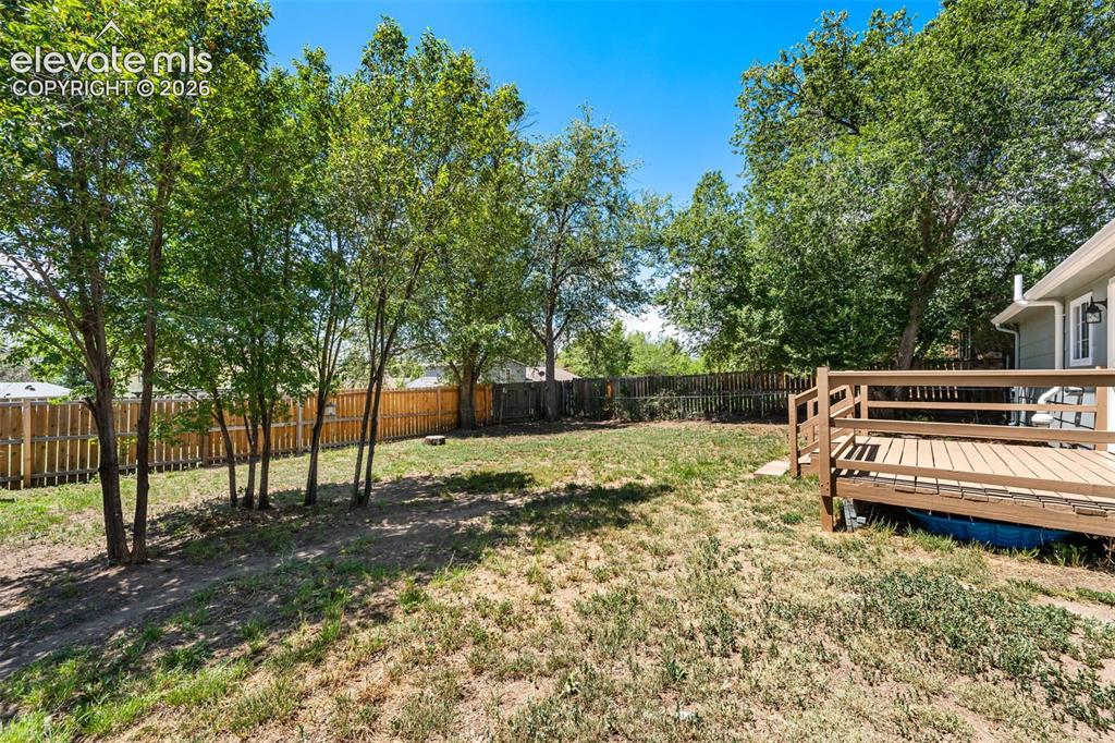 Image 35 of 39: Fenced backyard featuring a wood deck, mature trees, and a level lawn area
