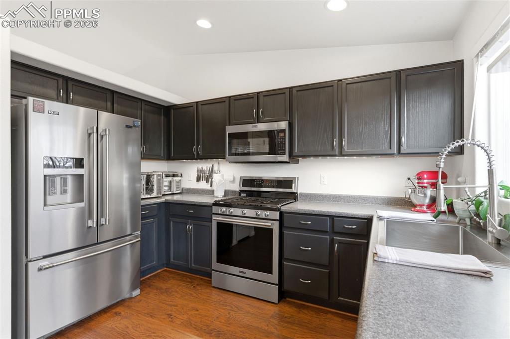 Image 12 of 44: Kitchen featuring stainless steel appliances, vaulted ceiling, dark wood-st
