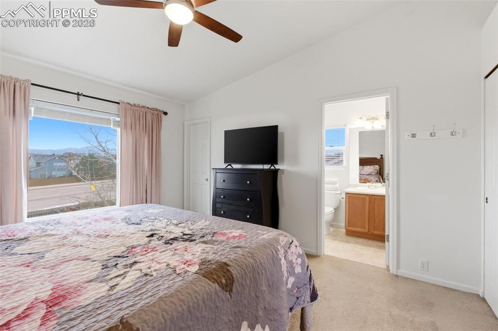 Image 24 of 44: Bedroom with vaulted ceiling, ceiling fan, light carpet, and connected bath