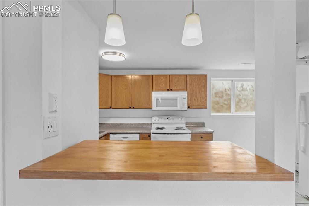 Image 6 of 17: Kitchen featuring white appliances, pendant lighting, and brown cabinets