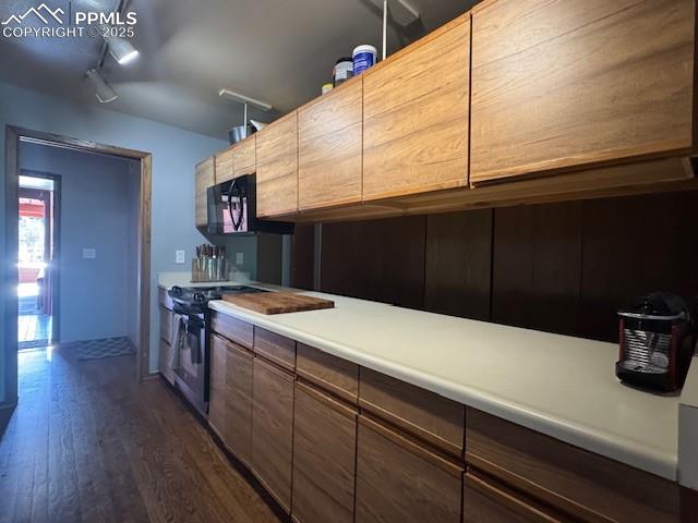 Image 16 of 17: Kitchen with dark wood finished floors, range, light countertops, track lig