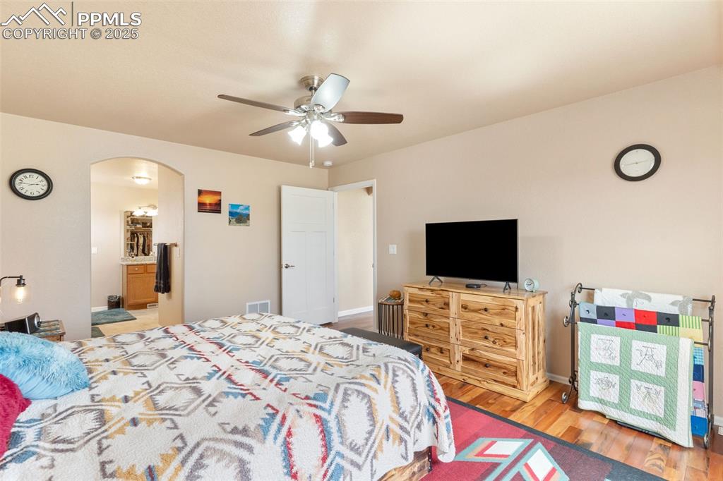 Image 16 of 33: Bedroom featuring arched walkways, wood finished floors, a ceiling fan, and
