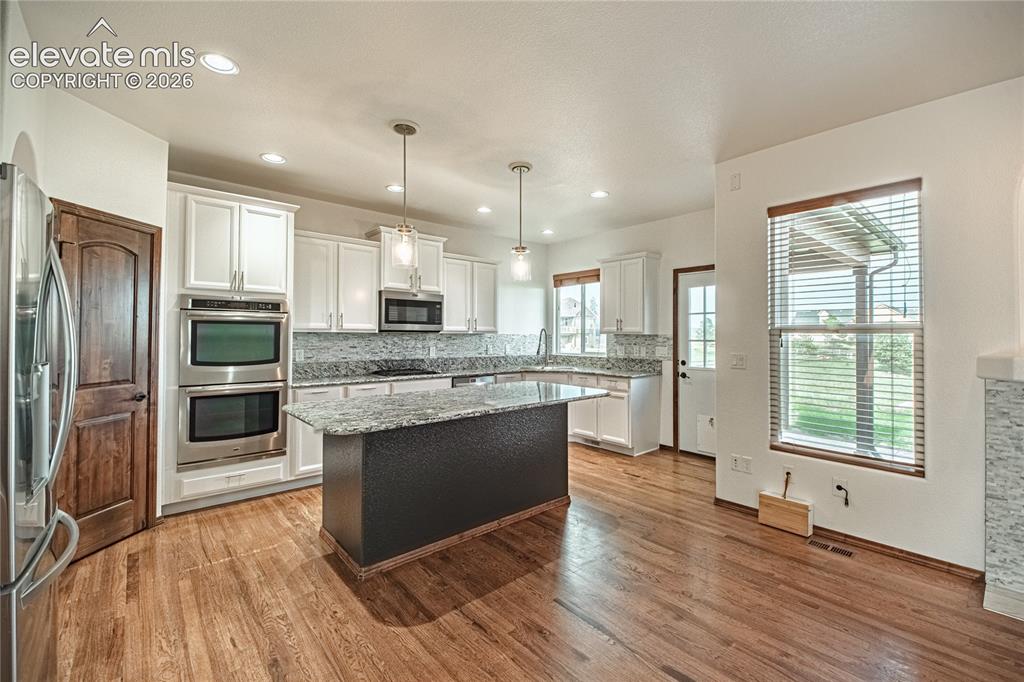 Image 14 of 38: Open-concept kitchen with wood-finish flooring, white cabinetry, and stainl