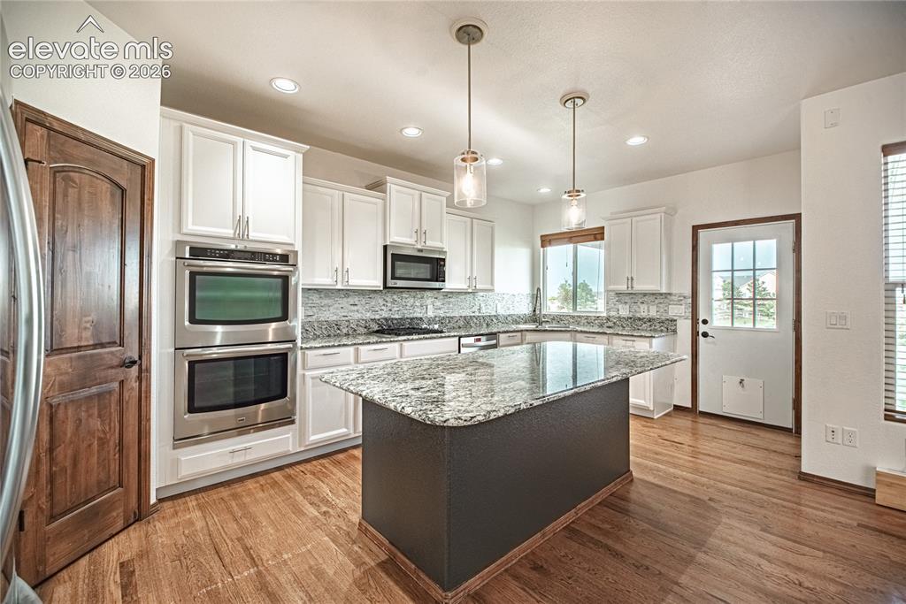 Image 15 of 38: Kitchen featuring a large island with a granite countertop, white cabinetry