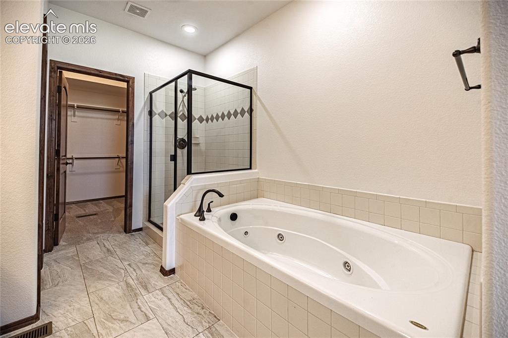 Image 24 of 38: Soaking tub with tiled surround, walk-in shower with glass enclosure and de