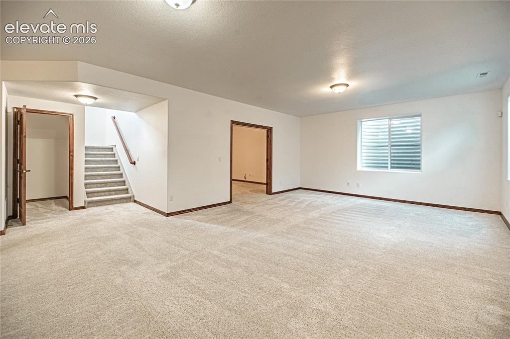 Image 29 of 38: Open-concept living area featuring light-toned carpeting, white walls, and