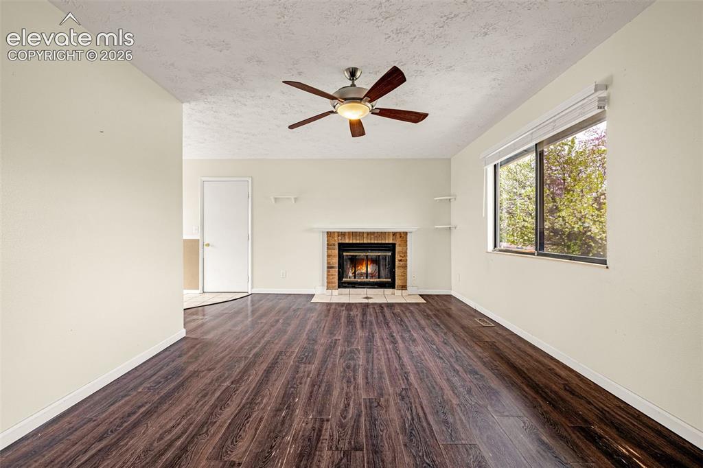 Image 4 of 20: Living room with wood-burning fireplace, ceiling fan, wood laminate floorin