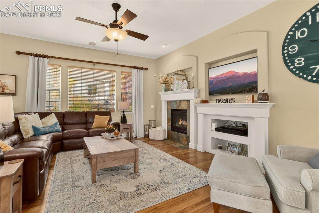 Image 11 of 40: Living area with a tiled fireplace, wood finished floors, and a ceiling fan