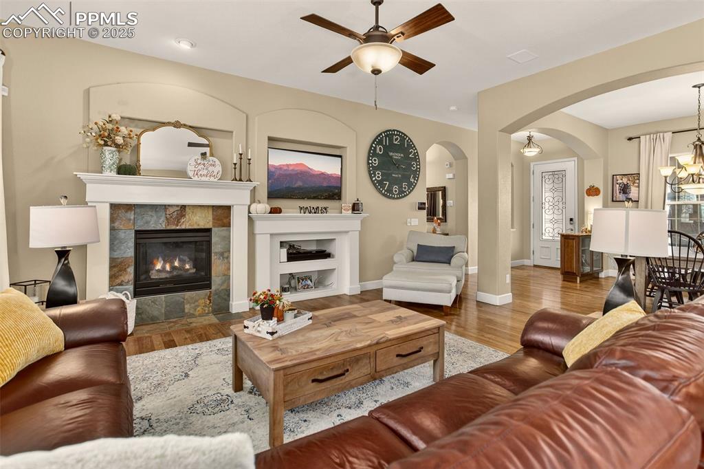 Image 13 of 40: Living room with a fireplace, ceiling fan, wood finished floors, a chandeli