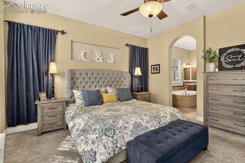 Image 18 of 40: Bedroom with light colored carpet, arched walkways, and ensuite bath