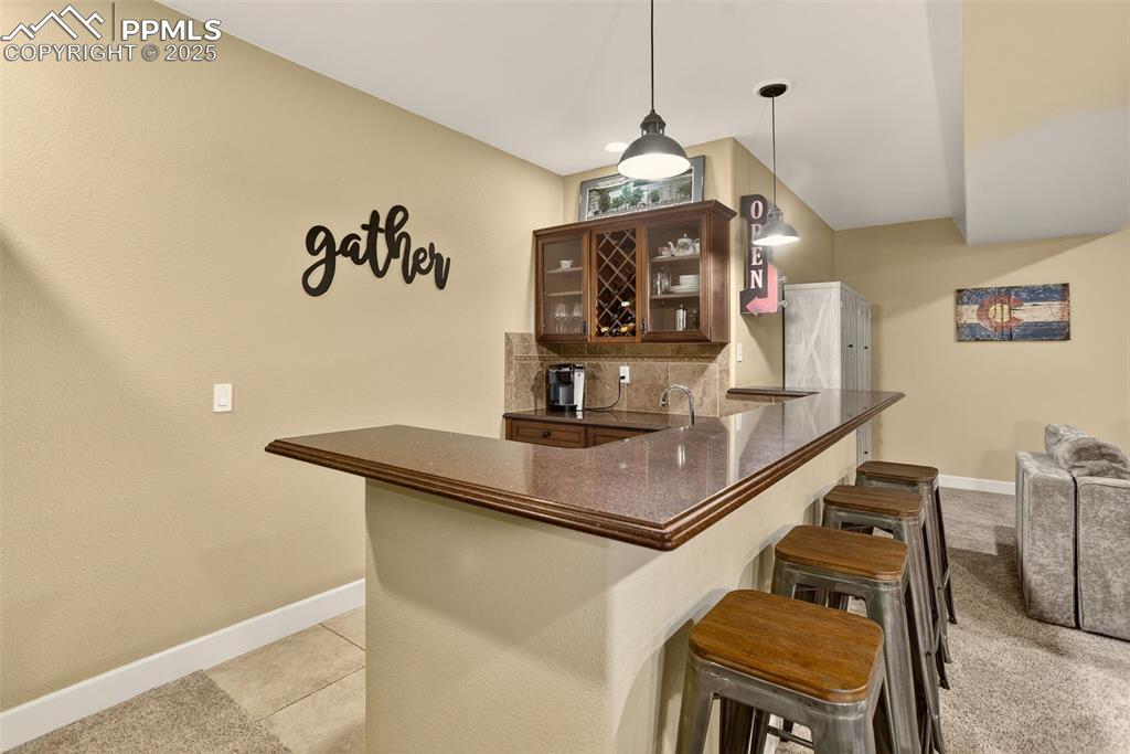 Image 26 of 40: Indoor wet bar featuring backsplash, glass insert cabinets, decorative ligh