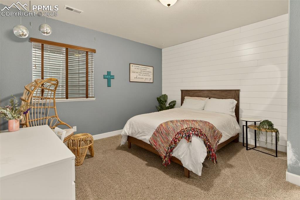 Image 27 of 40: Bedroom featuring light carpet, wooden walls, and an accent wall