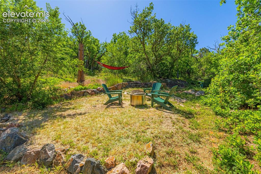 Image 17 of 21: Outdoor gathering area featuring a fire pit, three Adirondack chairs, and n
