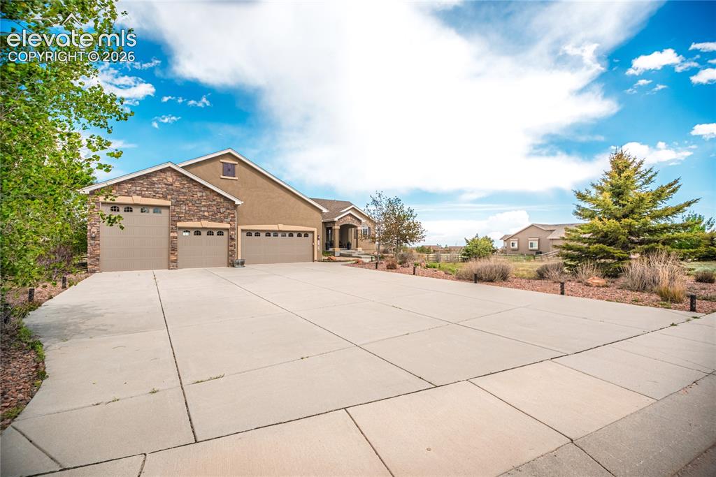 Image 2 of 50: Expansive concrete driveway leading to a residence featuring a stucco and s