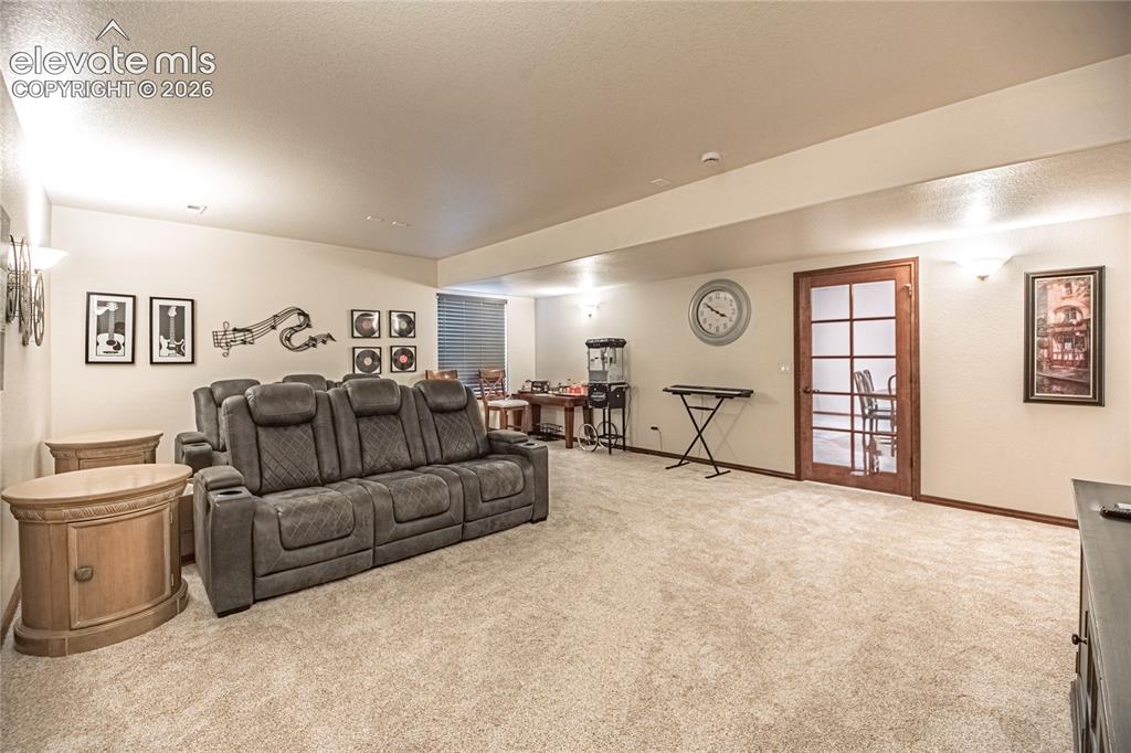 Image 31 of 50: Spacious lower-level room featuring light-toned carpet flooring, wall sconc