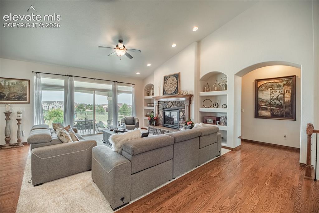 Image 6 of 50: Spacious living area featuring wood-finish flooring, a stone fireplace with