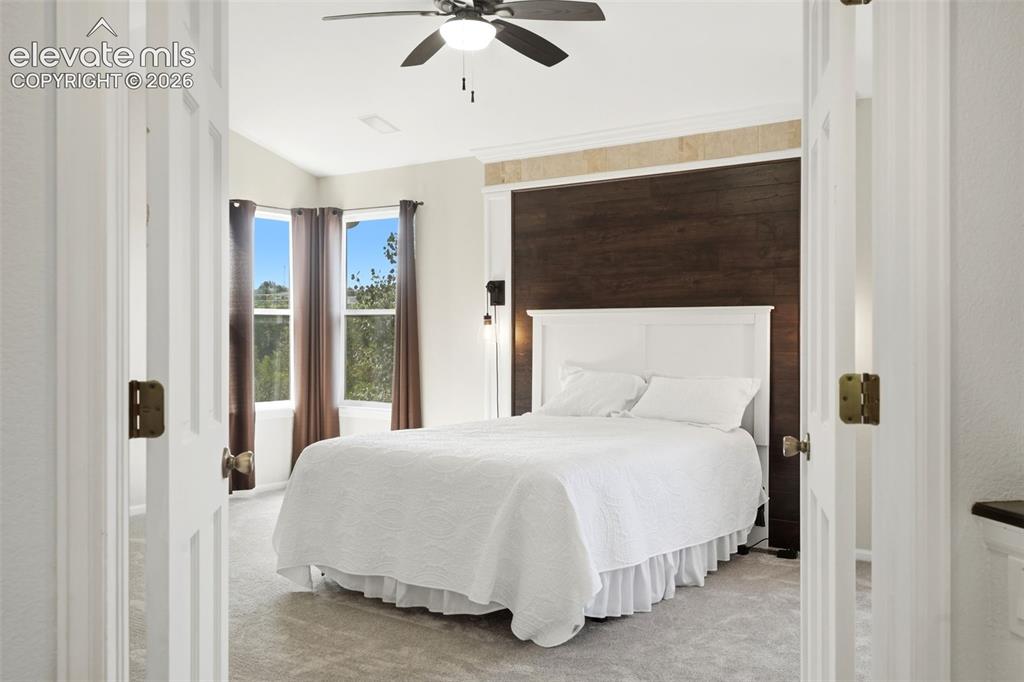 Image 18 of 43: Bedroom featuring a dark wood-finish accent wall, ceiling fan, and carpet f