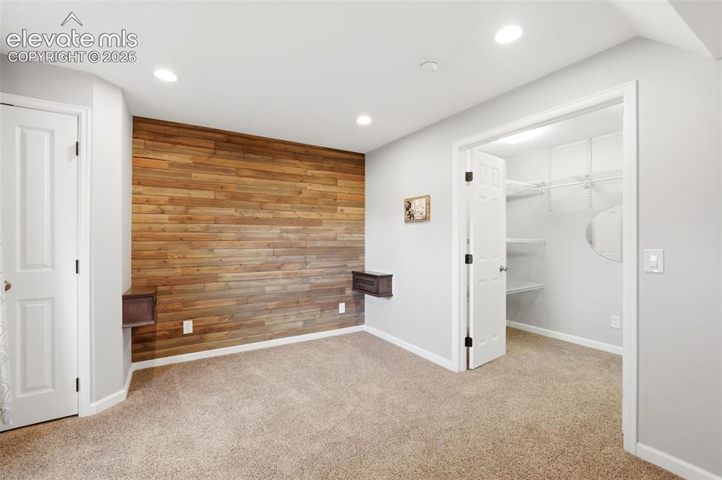 Image 32 of 43: Bedroom featuring a wood-panel accent wall, recessed lighting, and soft car
