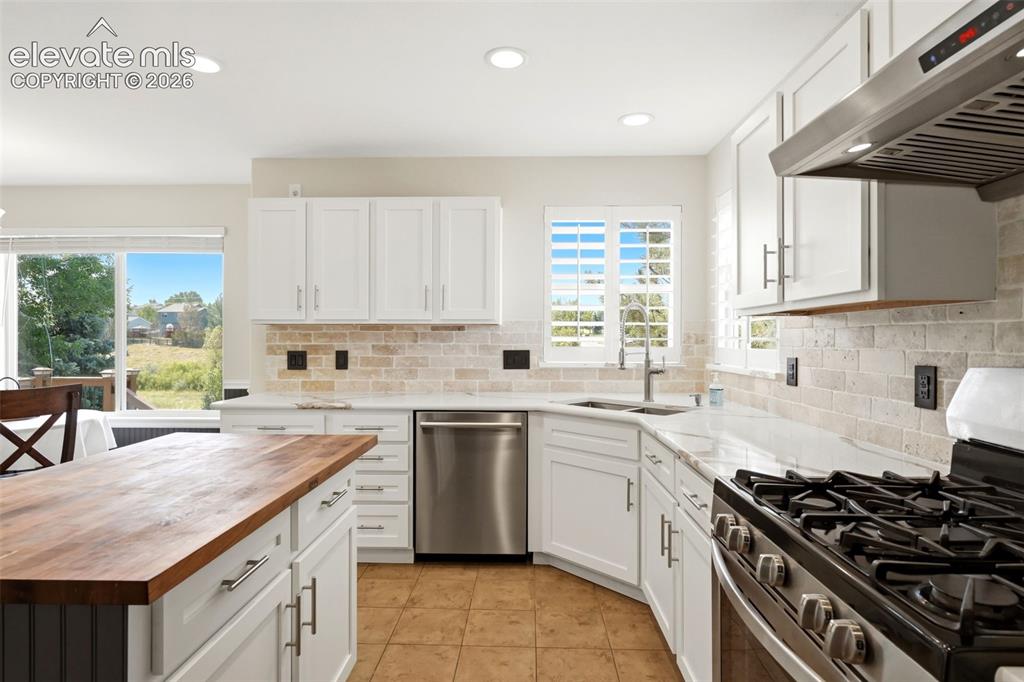 Image 8 of 43: Kitchen featuring white shaker cabinetry, light-toned tile backsplash, stai