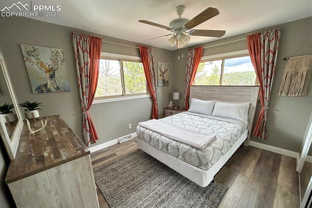 Image 17 of 50: Bedroom with dark wood finished floors, multiple windows, and a ceiling fan