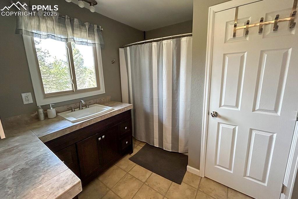 Image 20 of 50: Bathroom featuring vanity, light tile patterned floors, and a shower with c