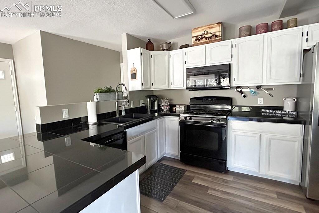Image 7 of 50: Kitchen featuring dark countertops, black appliances, white cabinets, a tex