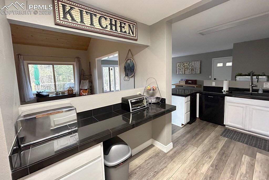 Image 8 of 50: Kitchen with dark countertops, white cabinetry, and light wood finished flo