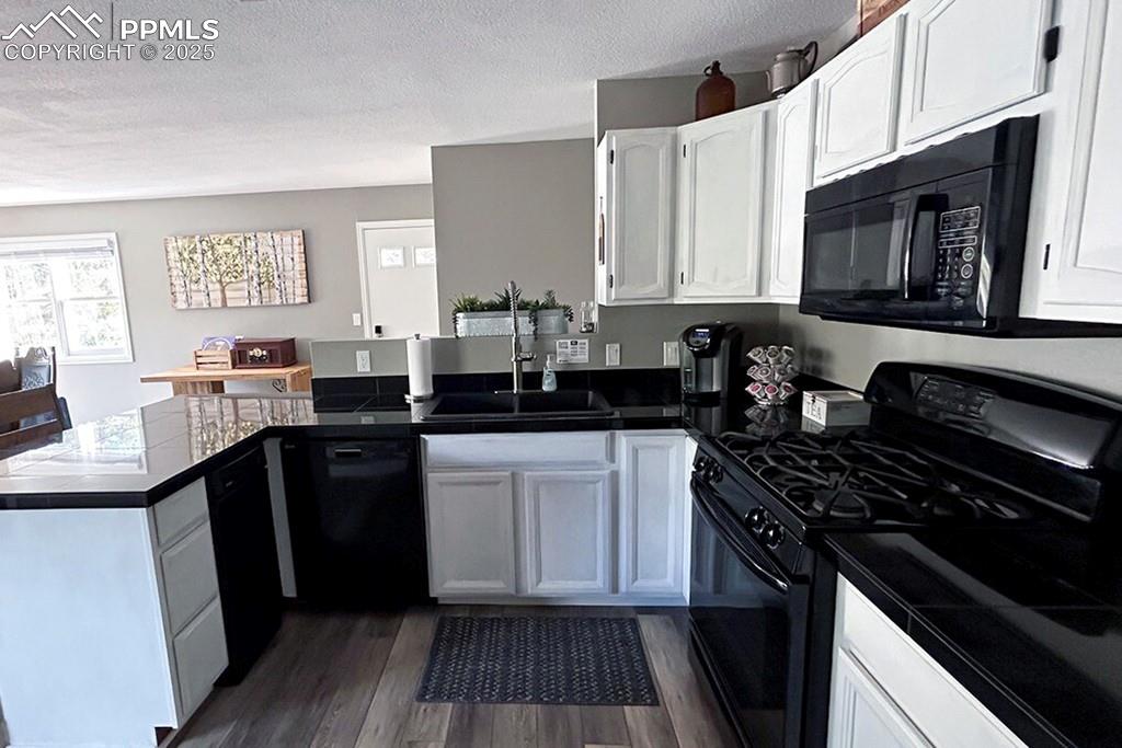 Image 9 of 50: Kitchen with black appliances, a peninsula, a textured ceiling, dark wood-s