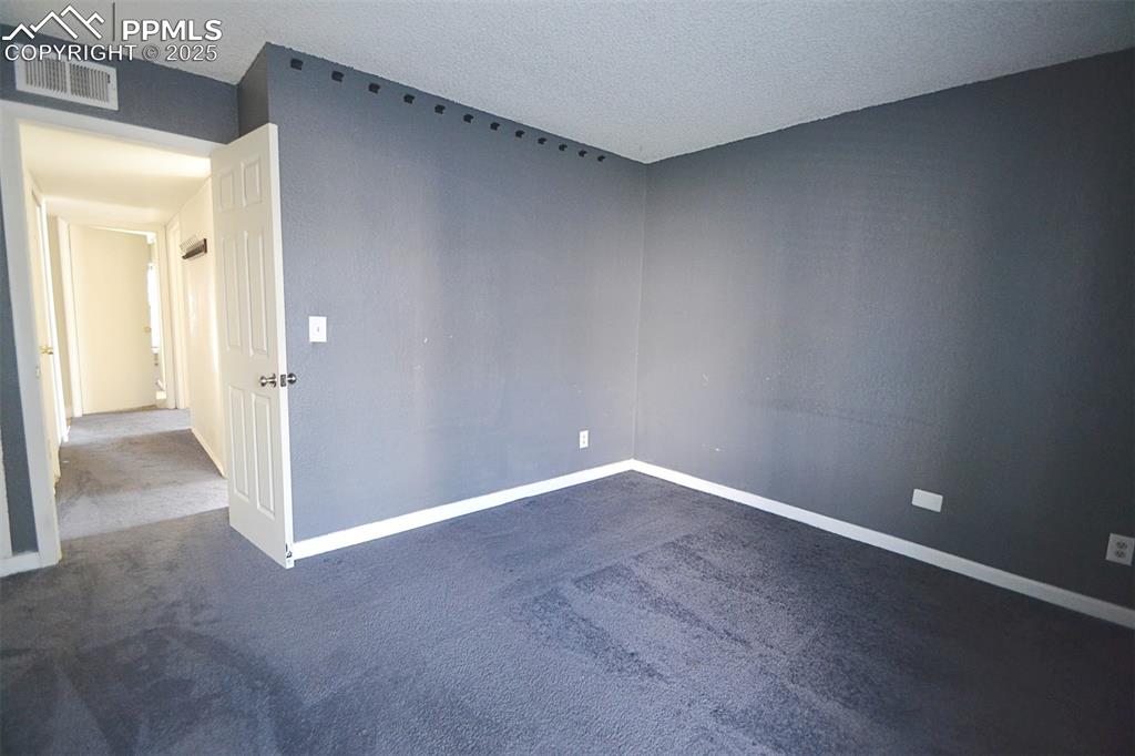 Image 28 of 31: Unfurnished room with dark colored carpet and a textured ceiling
