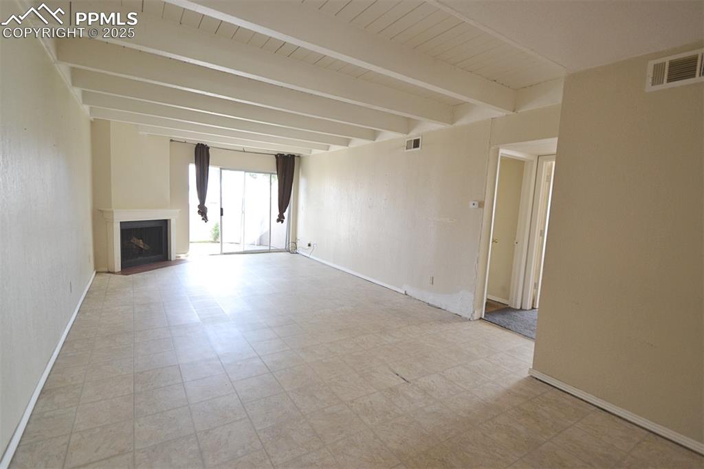 Image 7 of 31: Unfurnished living room with beamed ceiling and a fireplace