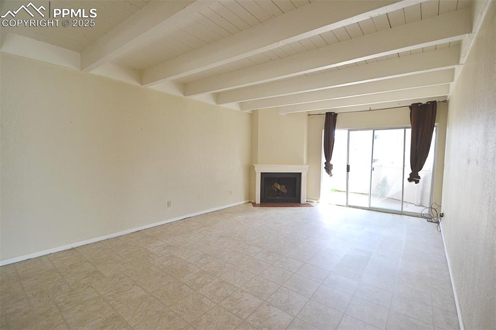 Image 8 of 31: Unfurnished living room featuring beam ceiling, a fireplace, and tile patte