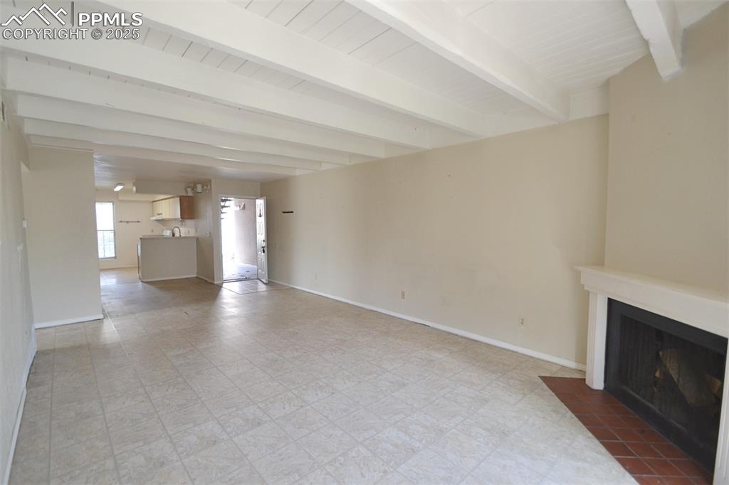 Image 9 of 31: Unfurnished living room featuring beamed ceiling, a fireplace with flush he
