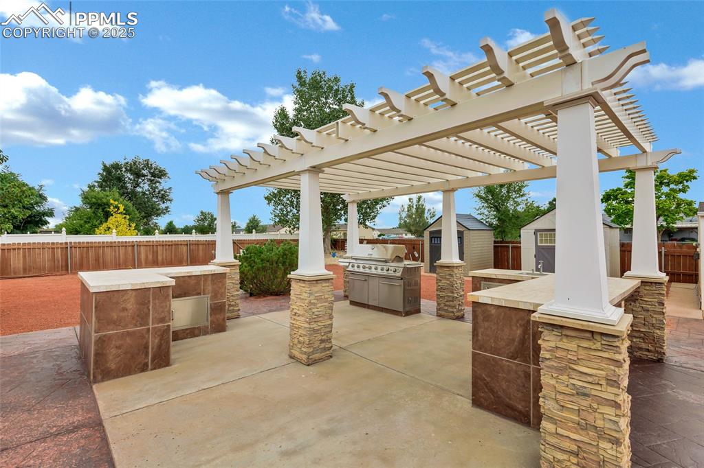 Image 20 of 39: Covered patio with Propane grill, frig, sink and a pergola