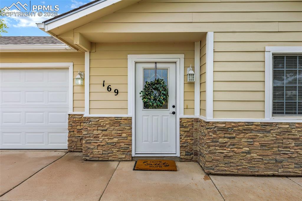 Image 4 of 39: View of exterior entry featuring stone siding, a garage, and concrete drive