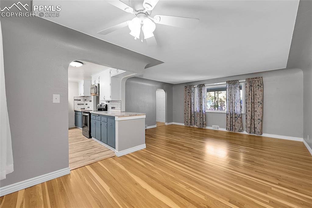 Image 4 of 27: Unfurnished living room with arched walkways, ceiling fan, and light wood f