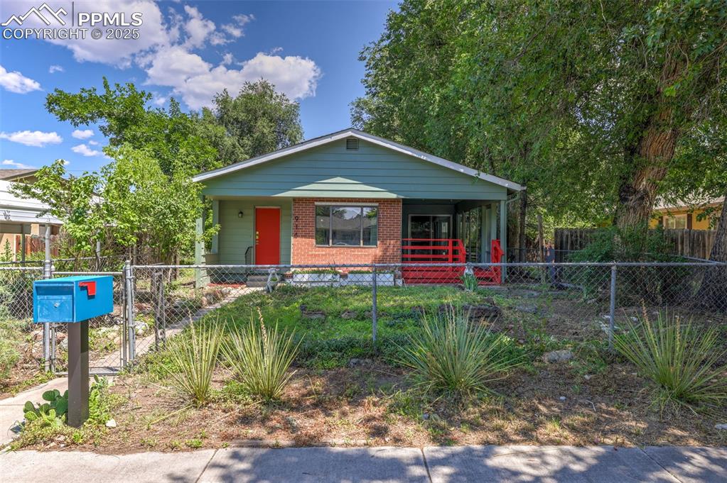 Caption: Bungalow-style home with covered porch, brick siding, a fenced front yard, and a gate