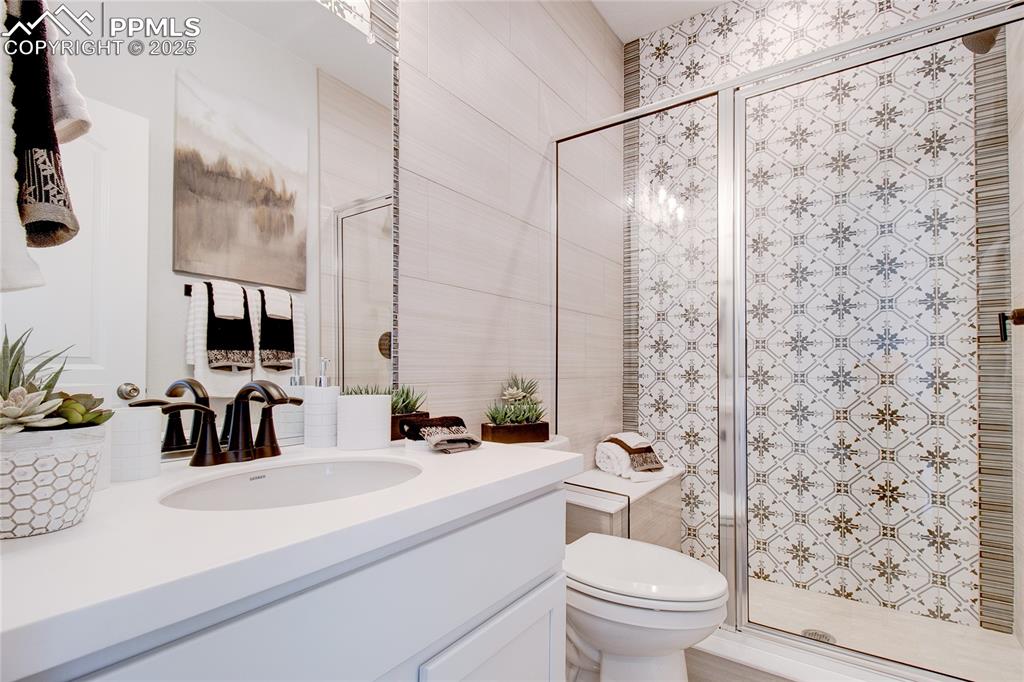 Image 17 of 32: Bathroom featuring toilet, tile walls, vanity, and a stall shower