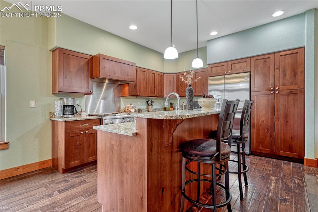 Image 14 of 43: Kitchen with dark wood finished floors, a kitchen bar, light stone counters