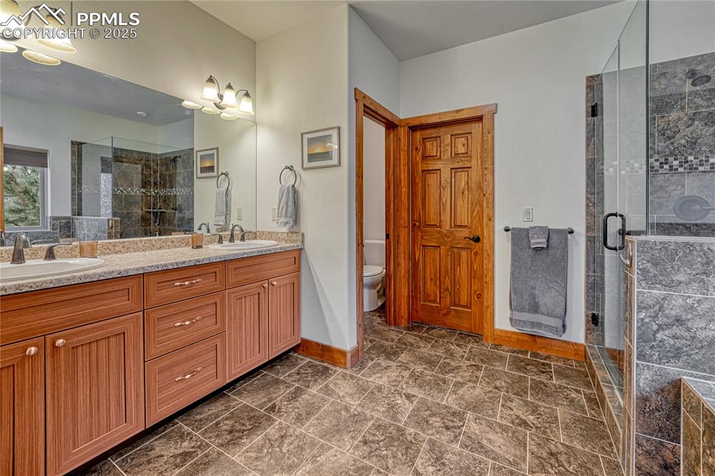 Image 24 of 43: Bathroom with double vanity, a shower stall, baseboards, and toilet