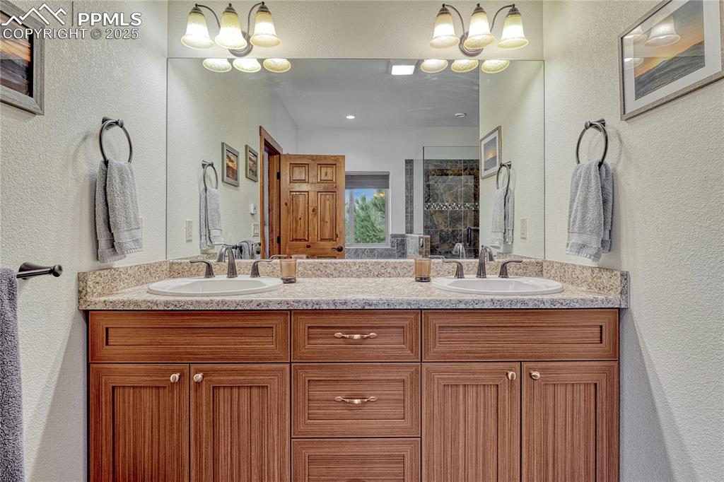 Image 26 of 43: Bathroom with double vanity, a textured wall, tiled shower, and a chandelie