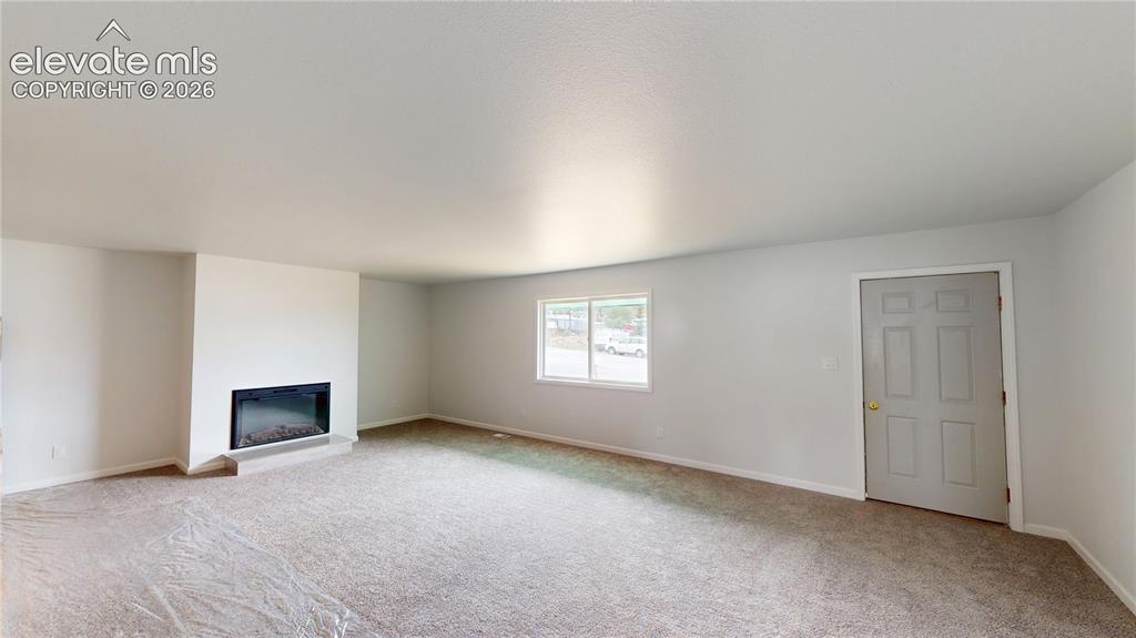 Image 6 of 16: Spacious room featuring neutral carpet, light-colored walls, a built-in fir